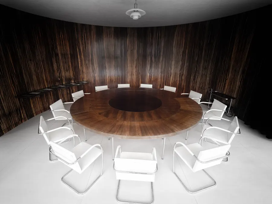 The round dining table and white Brno chairs inside the curved wall of dark striped Macassar ebony