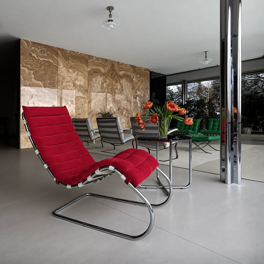 The honey-coloured onyx wall at Villa Tugendhat with a red lounge chair in front of it